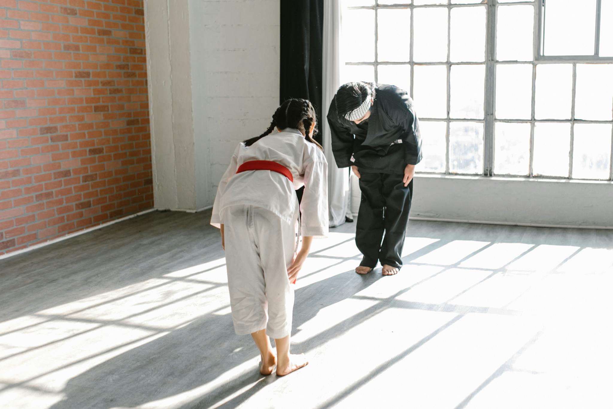A child and instructor bowing during martial arts training in a brightly lit dojo.