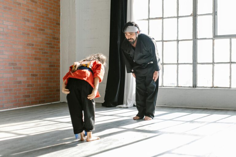 A martial arts instructor and student bowing indoors during training session.