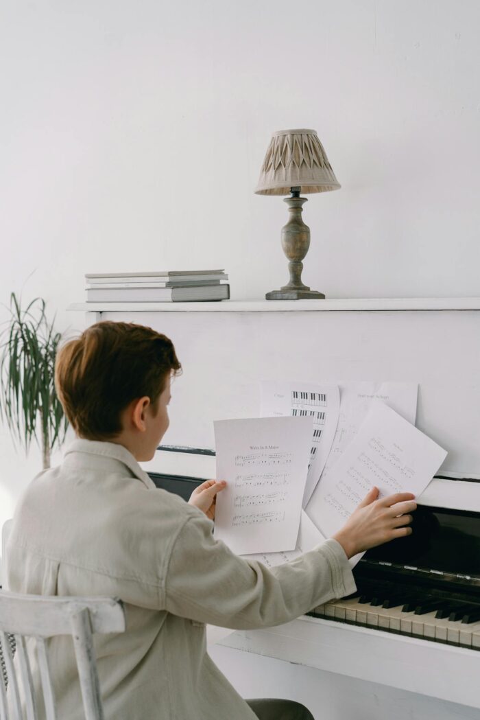 A young boy organizes sheet music while sitting at a piano, indicating his passion for music.