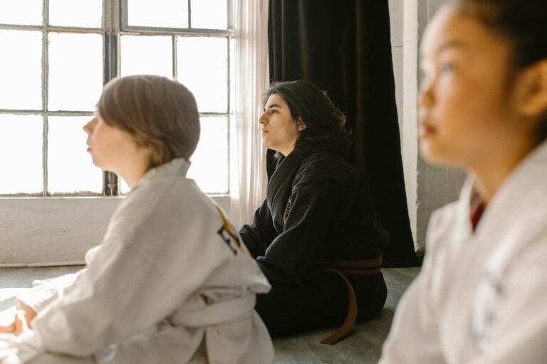 Children attentively listening in a martial arts dojo, wearing traditional uniforms.
