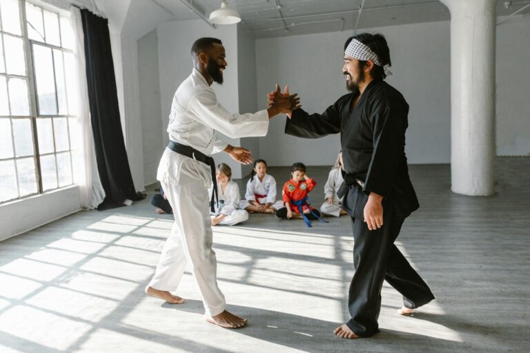Two martial arts instructors demonstrating a handshake of respect in a sunlit dojo while students observe.